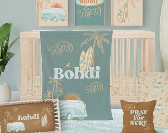 May include: A nursery room decorated in a beach theme with a crib, a blanket, pillows, and wall art. The blanket is teal blue with a palm tree, surfboard, and waves. The pillows are brown and beige with a surfboard, palm tree, and the text "Bohdi" and "Pray for Surf". The wall art features a teal blue background with a surfboard, palm tree, and the text "Bohdi".