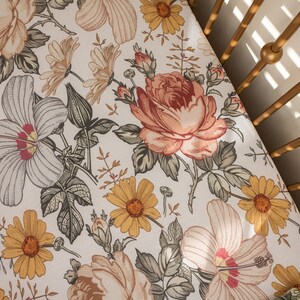 Op de afbeelding: Een wit babybeddengoed met een bloemenpatroon met gele, roze en groene bloemen. Het laken is gemaakt van zachte, ademende stof en is perfect voor een babybed.