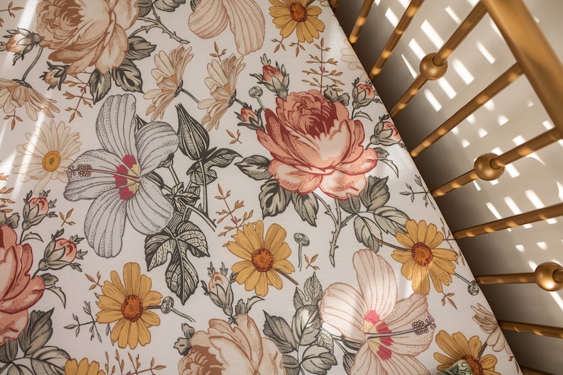 Op de afbeelding: Een wit babybeddengoed met een bloemenpatroon met gele, roze en groene bloemen. Het laken is gemaakt van zachte, ademende stof en is perfect voor een babybed.