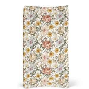 Op de afbeelding: Een witte stoffen tas met een bloemenpatroon met roze, gele en groene bloemen. De tas heeft een gebogen bodem en een witte achtergrond.