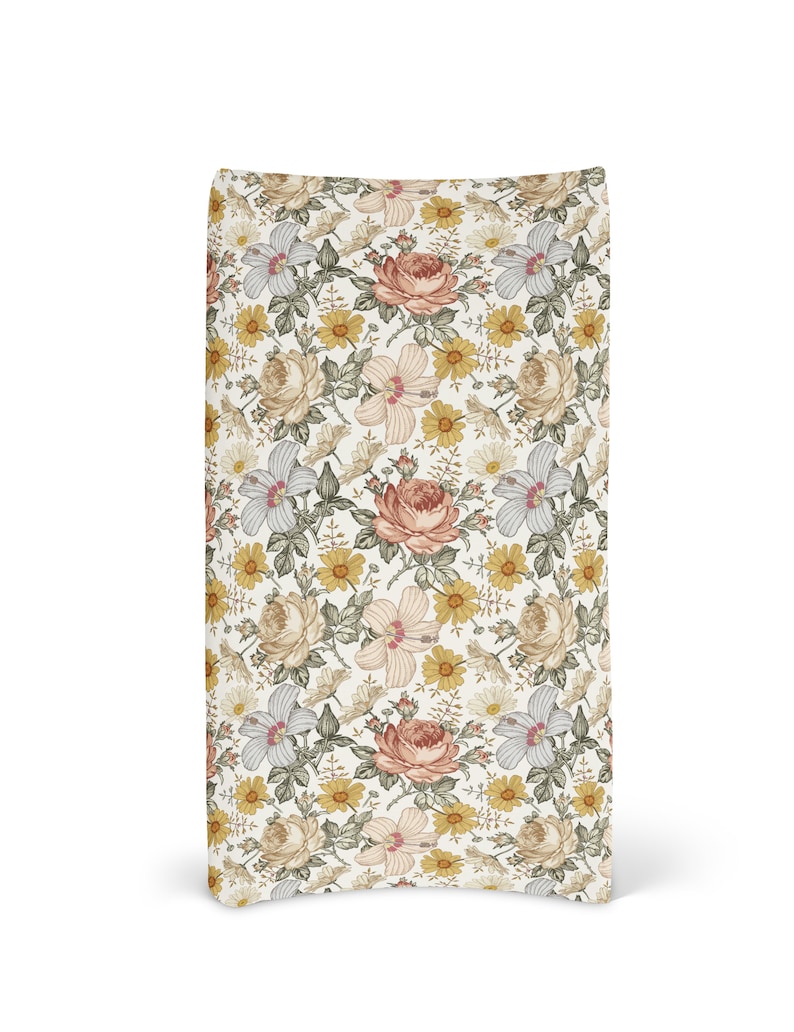 Op de afbeelding: Een witte stoffen tas met een bloemenpatroon met roze, gele en groene bloemen. De tas heeft een gebogen bodem en een witte achtergrond.