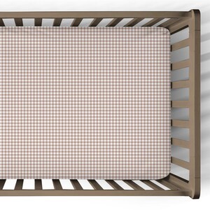 May include: A fitted crib sheet with a brown and white gingham pattern. The sheet is made of a soft fabric and is designed to fit a standard crib mattress. The crib is made of wood.