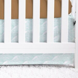 May include: White crib with a brown fitted sheet and a turquoise and white wave patterned crib skirt.