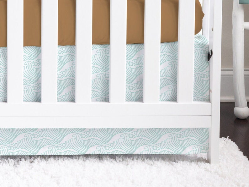 May include: White crib with a brown fitted sheet and a turquoise and white wave patterned crib skirt.