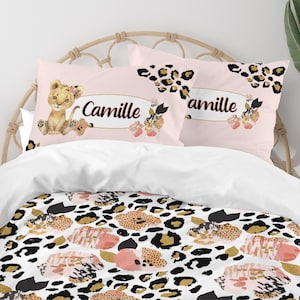 May include: Pink and white bedding set with a leopard print design. The set includes two pillowcases with a pink background and a lion cub illustration. One pillowcase has the name "Camille" printed on it.
