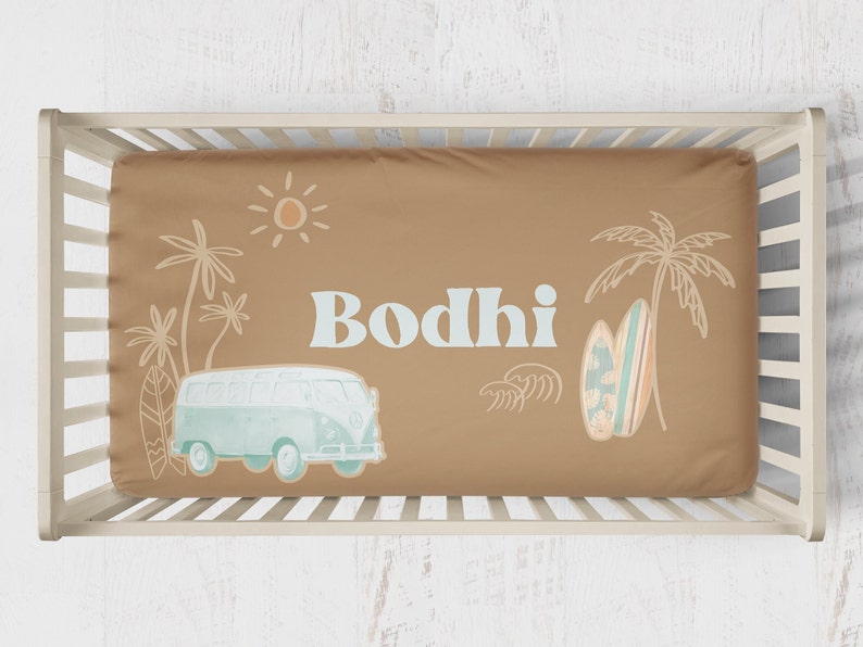 May include: A tan crib sheet with a light blue and white illustration of a vintage van, palm trees, a surfboard, and the name "Bodhi".