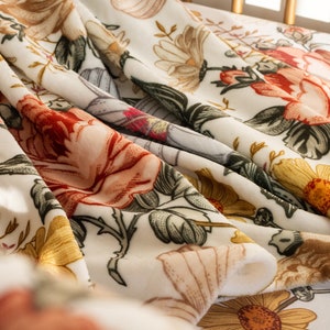 May include: A white fabric with a floral pattern featuring red, yellow, and green flowers. The fabric is folded and draped over a surface.