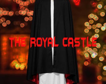 Puede incluir: Una capa negra con forro rojo y un broche dorado. La capa se lleva sobre una prenda blanca. El texto "THE ROYAL CASTLE" se muestra en rojo en la imagen. La capa tiene una capucha.