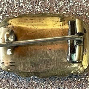 May include: A vintage-style brooch with a rectangular shape, featuring a gold-toned metal frame and a pin closure on the back. The brooch has a textured surface and a classic design, suitable for adding a touch of elegance to any outfit.