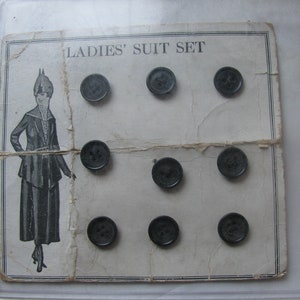 May include: A card with the text "LADIES' SUIT SET" printed on it. There are ten black buttons arranged in a grid pattern on the card.
