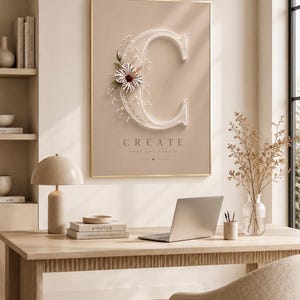 Könnte beinhalten: Ein gerahmter Wandkunstdruck mit einem großen, weißen, dreidimensionalen Buchstaben C, der mit einer weiß-kastanienbraunen Hibiskusblüte und kleinen Schleierkraut-Zweigen verziert ist. Unter dem Buchstaben steht der Text CREATE your own beauty.