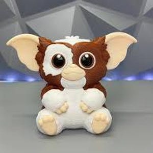 May include: A Gremlins-themed figurine featuring a brown and white creature with large ears and big eyes. The figurine has a detailed design with a textured appearance and is sitting down.