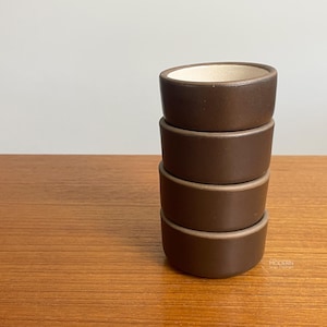 May include: A stack of four small, round ceramic bowls with a smooth, dark brown exterior finish and a contrasting off-white interior. The bowls are uniform in size and shape, featuring a simple, clean design with a matte texture throughout.