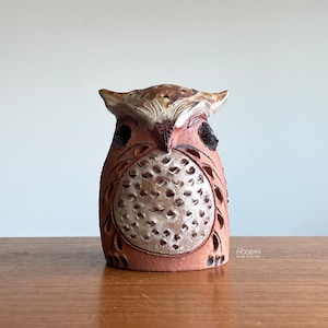 May include: A handcrafted ceramic owl figurine. The owl features a reddish-brown body with intricate cut-out patterns and a textured, off-white belly. The owl's head has a detailed feather design, and black accents highlight the eyes and other features.