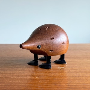 May include: A whimsical wooden figurine of a hedgehog with a brown body and black legs. The hedgehog has a long snout, small black eyes, and several small holes on its back. The figurine is standing on a wooden surface.