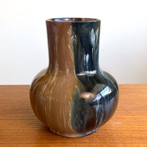May include: A ceramic vase with a bulbous body and a cylindrical neck, featuring a glossy glaze that transitions from a warm tan on the left to a deep, dark blue-black on the right, with white vertical streaks blending the two distinct colors.