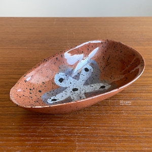 May include: A small, oval-shaped ceramic dish with a speckled, reddish-brown exterior. The interior features a white and gray abstract design with black accents. The dish is likely for decorative or serving purposes.
