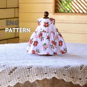 Peut inclure: Une robe blanche ornée d'un motif floral de roses rouges et roses. La robe est présentée sur un support en bois. Le texte "ENG PATTERN" est visible.