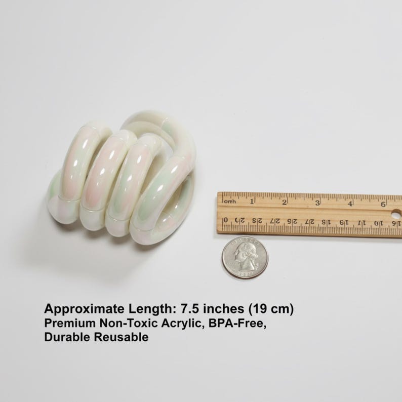 May include: A white and iridescent acrylic toy, approximately 19 cm long, with a spiral design. The toy has subtle pink and green hues. A ruler and a coin are next to the toy for size comparison.