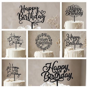 Puede incluir: Una colección de adornos para tartas de acrílico negro con las palabras "Happy Birthday" en varias fuentes elegantes. Algunos adornos presentan elementos decorativos como corazones, hojas y coronas florales. Los adornos se muestran en pasteles glaseados blancos.