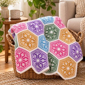 May include: A handmade crochet blanket featuring a repeating pattern of colorful hexagonal motifs in shades of pink, purple, blue, green, and yellow, each with a white star-like center, resting inside a woven wicker basket.