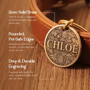 May include: A round solid brass pet tag featuring the name CHLOE engraved in the center against a detailed floral pattern. The tag is attached to a brown leather collar with a gold-toned metal ring and has smooth, rounded edges.