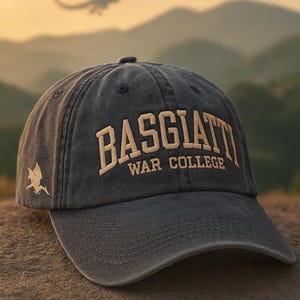 May include: A dark gray baseball cap with the text "BASGIATT WAR COLLEGE" embroidered in tan. A dragon silhouette is visible in the background. The cap has a curved brim and a small dragon emblem on the side.