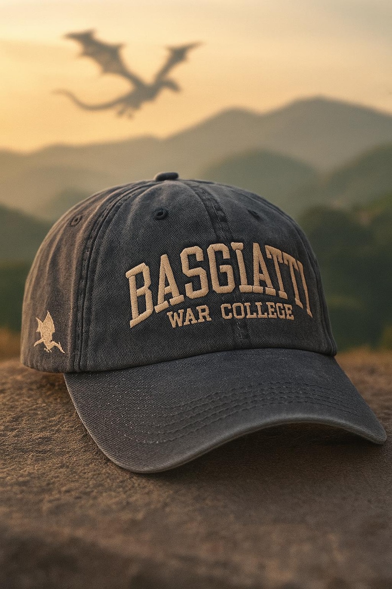 May include: A dark gray baseball cap with the text "BASGIATT WAR COLLEGE" embroidered in tan. A dragon silhouette is visible in the background. The cap has a curved brim and a small dragon emblem on the side.