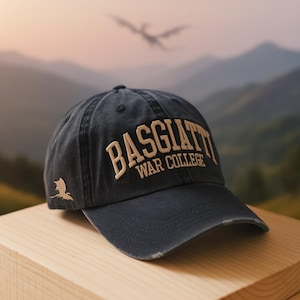 May include: A navy blue baseball cap with the text "BASGIATTI WAR COLLEGE" embroidered in tan. A small tan dragon emblem is on the side. The cap has a distressed look.