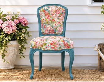 May include: A teal painted wooden chair with curved legs and an upholstered backrest and seat featuring a colorful floral pattern with pink, red, and white flowers on a light blue background. The chair has a rounded back frame.