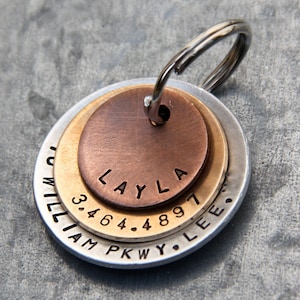 May include: A silver, gold, and copper layered dog tag with the name "LAYLA" engraved on the copper layer. The tag also has the address "3464. 4897 WILLIAM PKWY. LEE." engraved on the silver layer.