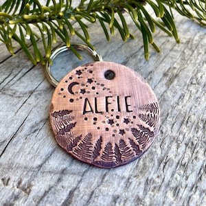 Puede incluir: Chapa de perro de cobre con un diseño de helecho y luna. La chapa está grabada con el nombre "Alfie".