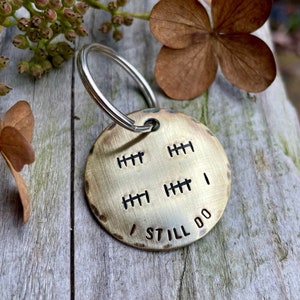 May include: A brass keychain with a round tag that says "I Still Do" and has four rows of hash marks. The keychain has a silver ring.