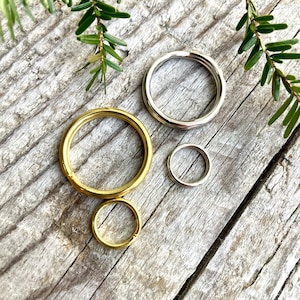 May include: Three metal key rings in different sizes. The largest ring is gold, the middle ring is silver, and the smallest ring is gold.