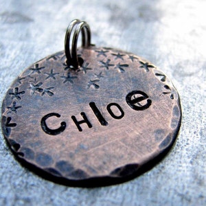 May include: A copper dog tag with a hammered finish and a starburst design around the edge. The tag is engraved with the name "Chloe".