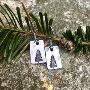 May include: A pair of silver earrings featuring a tree design. The earrings are hanging from a branch.