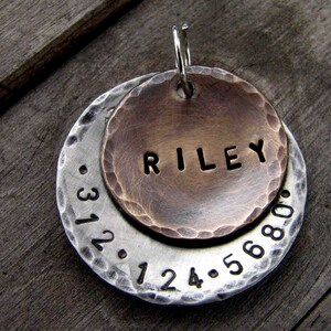 1" Aluminum disc hand stamped with a phone number is behind a 3/4" bronze pet tag stamped with the name "Riley" . Tag hangs from a small split ring.