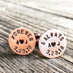 May include: A pair of copper cufflinks engraved with the words "Forever & Always". The cufflinks also feature the initials "A & J" and the date "3.23.18".