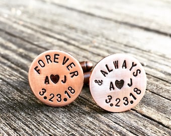 May include: A pair of copper cufflinks with the words "Forever & Always" engraved on them. The cufflinks also feature the initials "A & J" and the date "3.23.18".
