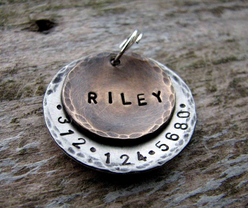 1" Aluminum disc hand stamped with a phone number is behind a 3/4" pet tag stamped with the name "Riley" . Tag hangs from a small split ring.