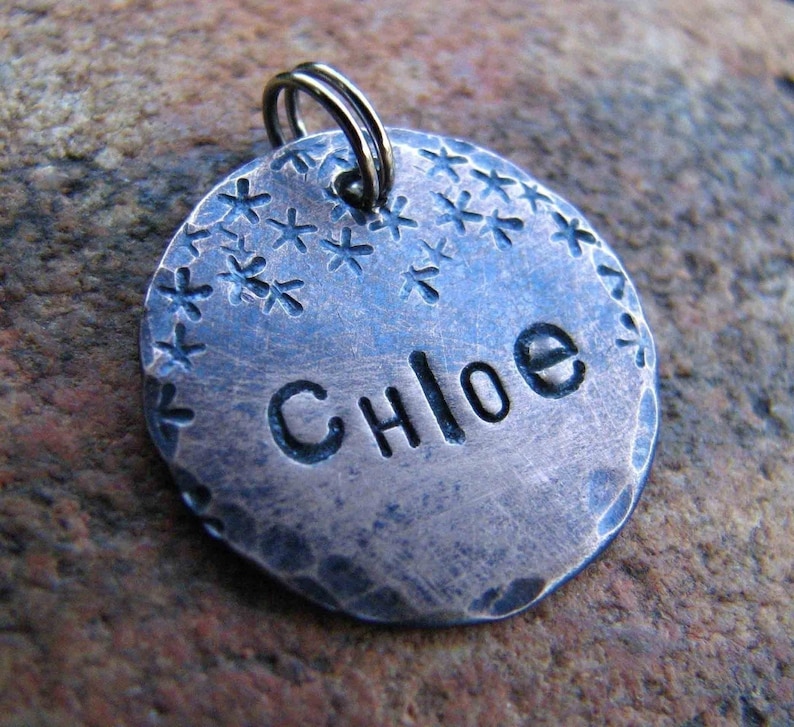 May include: A silver dog tag with a hammered finish and a starburst design around the edge. The name "Chloe" is engraved on the tag.