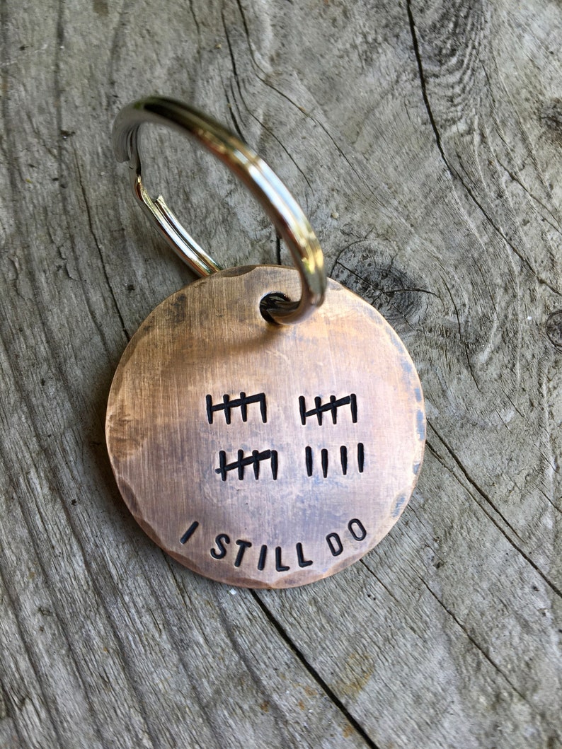 Peut inclure: Un porte-cl&eacute;s rond en laiton avec un anneau de cl&eacute; en argent. Le porte-cl&eacute;s comporte une s&eacute;rie de marques de pointage et les mots "I Still Do" grav&eacute;s dessus.