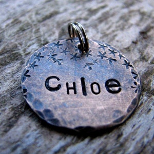 May include: A copper dog tag with a hammered finish and a starburst design. The tag is engraved with the name "Chloe".