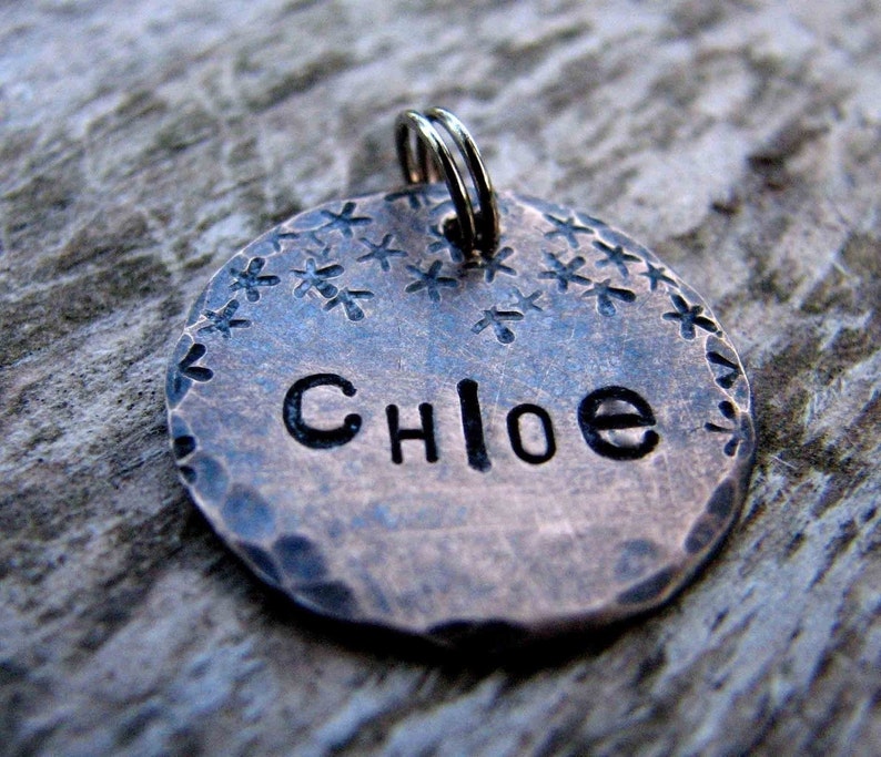 May include: A copper dog tag with a hammered finish and a starburst design. The tag is engraved with the name "Chloe".