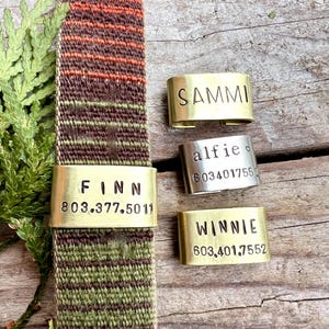 May include: A woven dog collar with a brass name tag that reads "FINN" and a phone number. Additional brass and silver name tags with pet names "SAMMI", "WINNIE", and "alfie" are also visible.