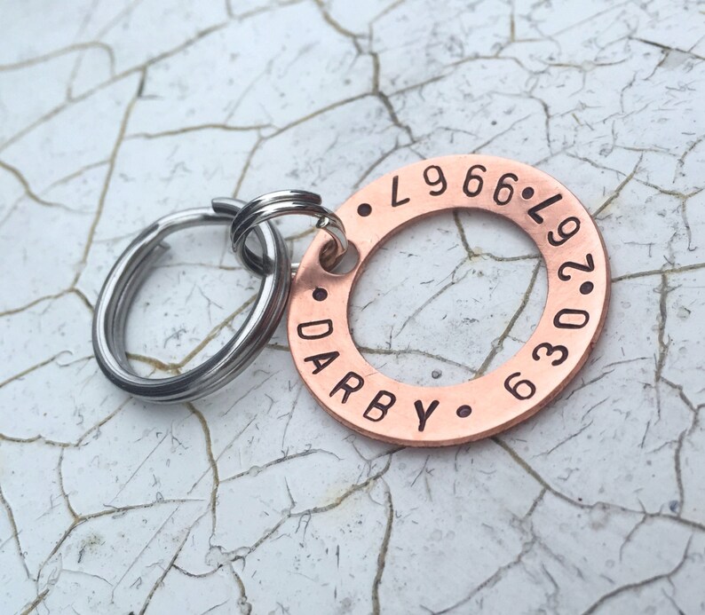 May include: Copper dog tag engraved with the text "DARBY" and "L.966.L.97.036". The tag is attached to a silver key ring.
