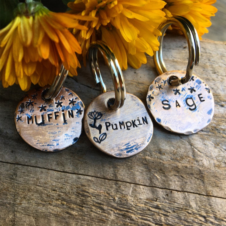 May include: Three round copper dog tags with key rings. The tags are engraved with the names "Muffin", "Pumpkin", and "Sage".