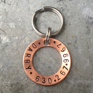 May include: A copper dog tag engraved with the name "Darby" and the phone number "630.267.9669". The tag is attached to a silver key ring.