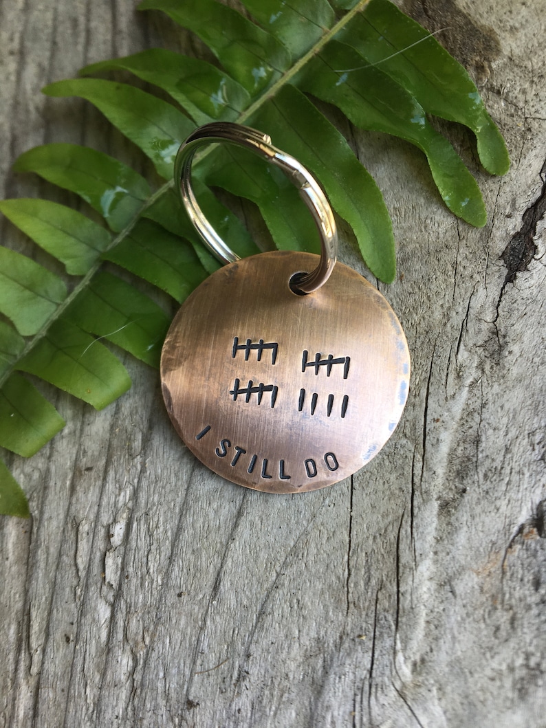 Peut inclure: Un porte-cl&eacute;s rond de couleur cuivre avec un anneau de cl&eacute; argent&eacute;. Le porte-cl&eacute;s comporte une s&eacute;rie de marques de pointage et le texte "I STILL DO" grav&eacute; dessus.