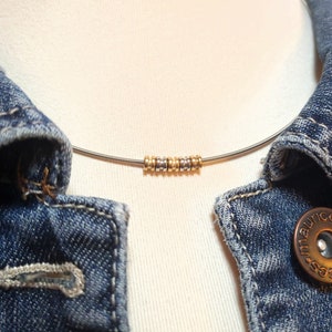 May include: A silver necklace with a row of small gold and silver beads. The necklace is on a white mannequin and a denim jacket.